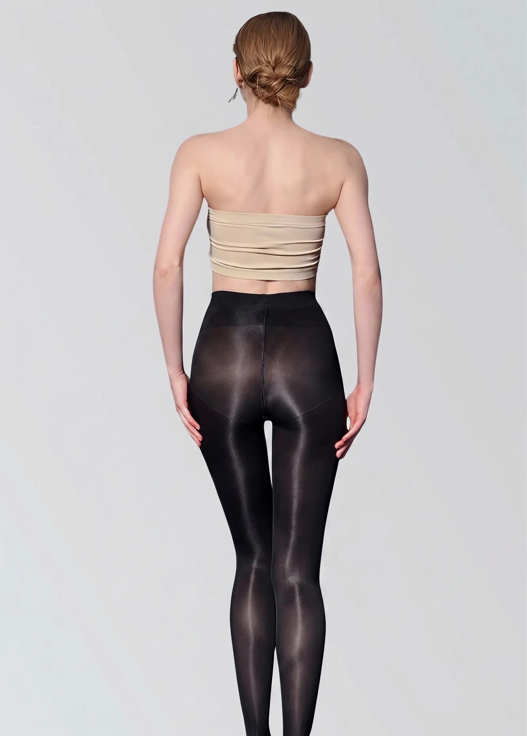 Woman wearing a beige strapless top and black tights on a plain background