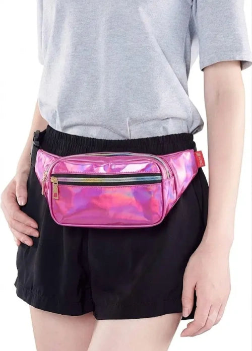 A person wearing a shiny holographic pink waist bag with a black elastic waistband, styled with a gray t-shirt and black shorts against a white background.