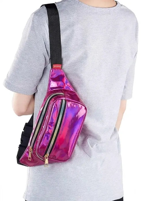 A person wearing a light gray t-shirt carries a shiny holographic pink and purple fanny pack with a black strap and gold zippers.