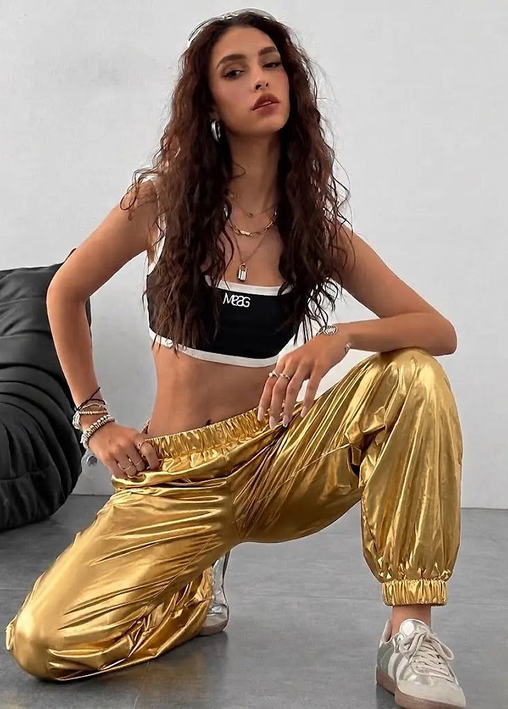 Woman wearing a black sports bra and gold pants sitting on the floor.
