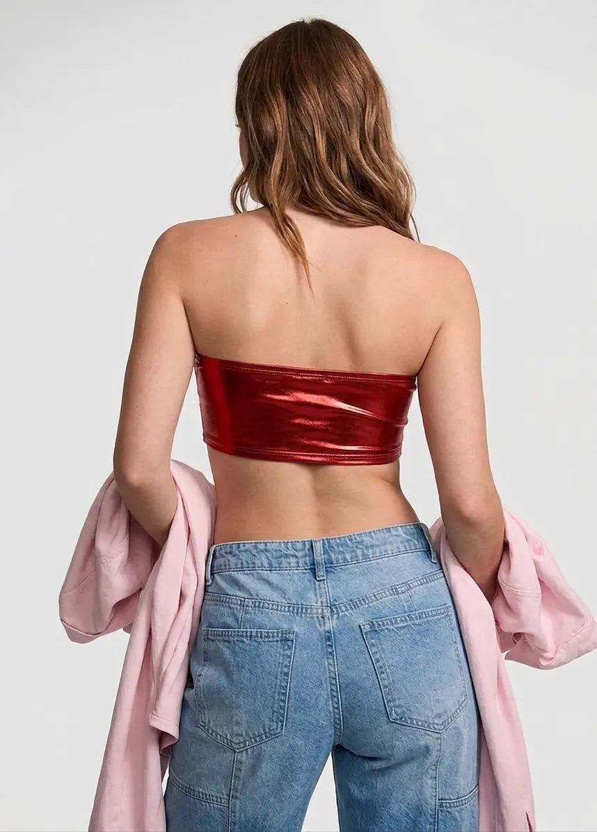 Woman wearing a red strapless top and blue jeans with a pink jacket over her shoulder on a light gray background